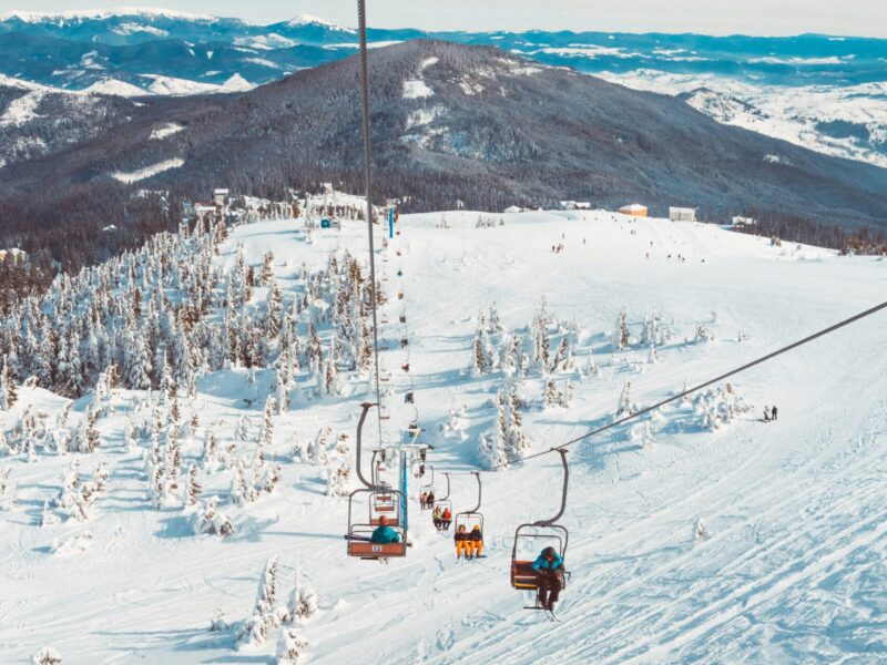 view down the slopes from a ski lift showing lift cars and people skiing below